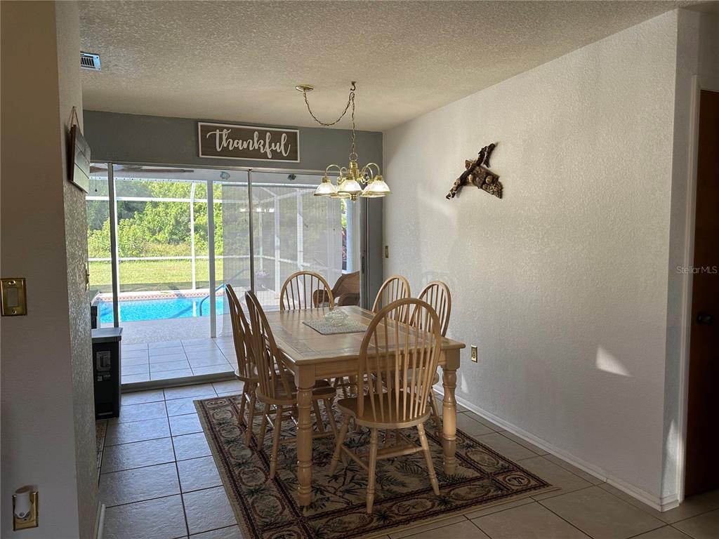 A dining room with a wooden table and chairs sits on a rug near a pool — 18625 ALPHONSE CIRCLE, PORT CHARLOTTE, FL
