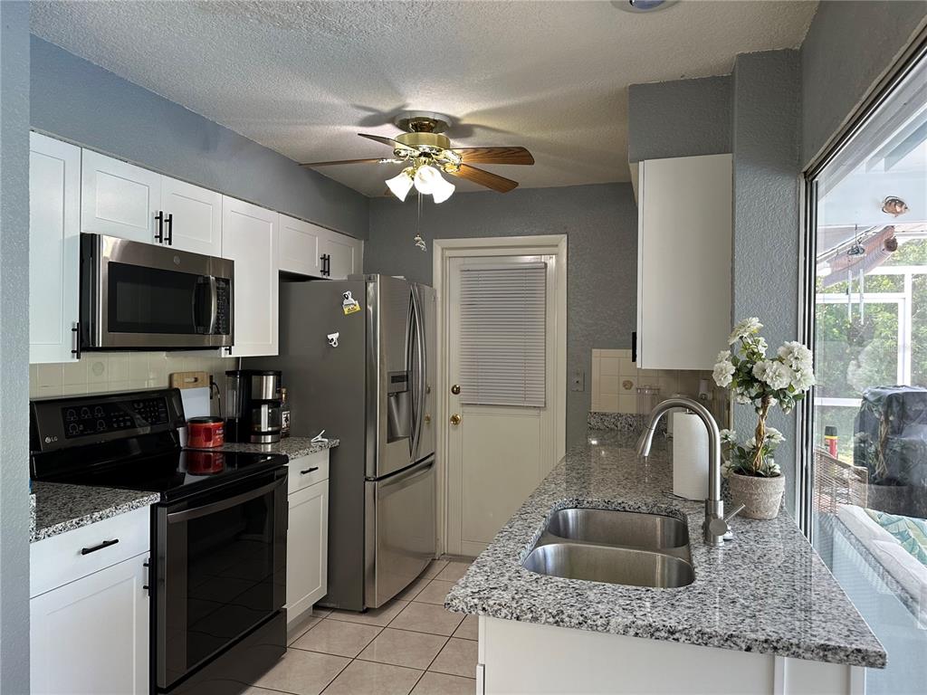 A kitchen features white cabinets, granite countertops, stainless steel appliances, and a ceiling fan — 18625 ALPHONSE CIRCLE, PORT CHARLOTTE, FL