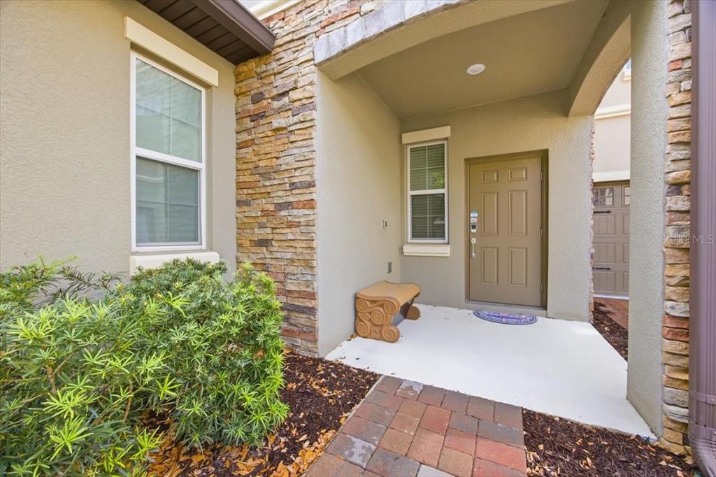 A covered entryway features a tan front door, stone accents, and a small decorative bench — 1365 SHINNECOCK HILLS DRIVE, DAVENPORT, FL