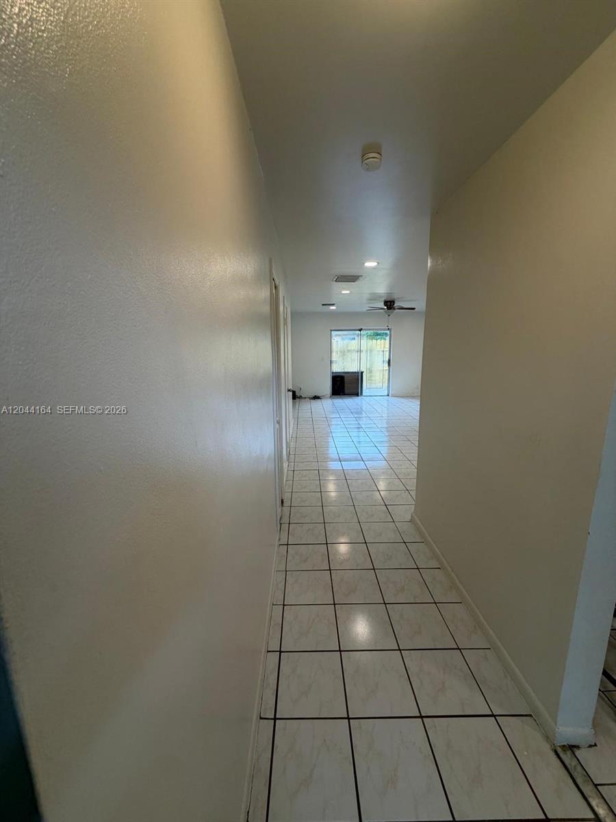 A long hallway with white tile flooring leads to a living area with sliding doors — 2065 NE 139th St, North Miami Beach FL 33181, NORTH MIAMI BEACH, FL
