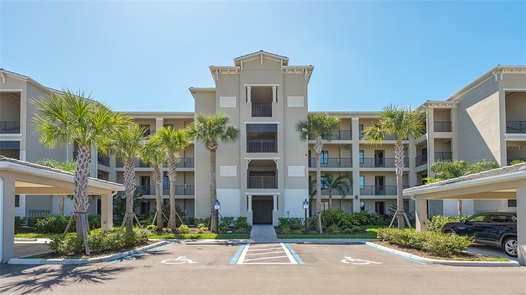 A multi-story apartment building exterior with palm trees and marked handicap parking spaces in front — 17902 GAWTHROP DRIVE UNIT 402, LAKEWOOD RANCH, FL