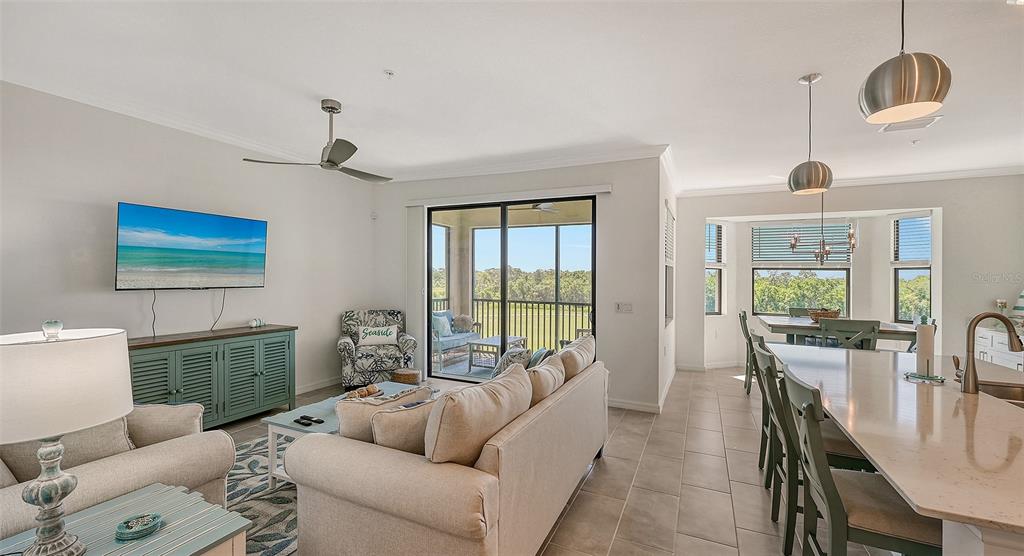 An open-concept living and dining area features a kitchen island, tile floors, and a balcony — 17902 GAWTHROP DRIVE UNIT 402, LAKEWOOD RANCH, FL