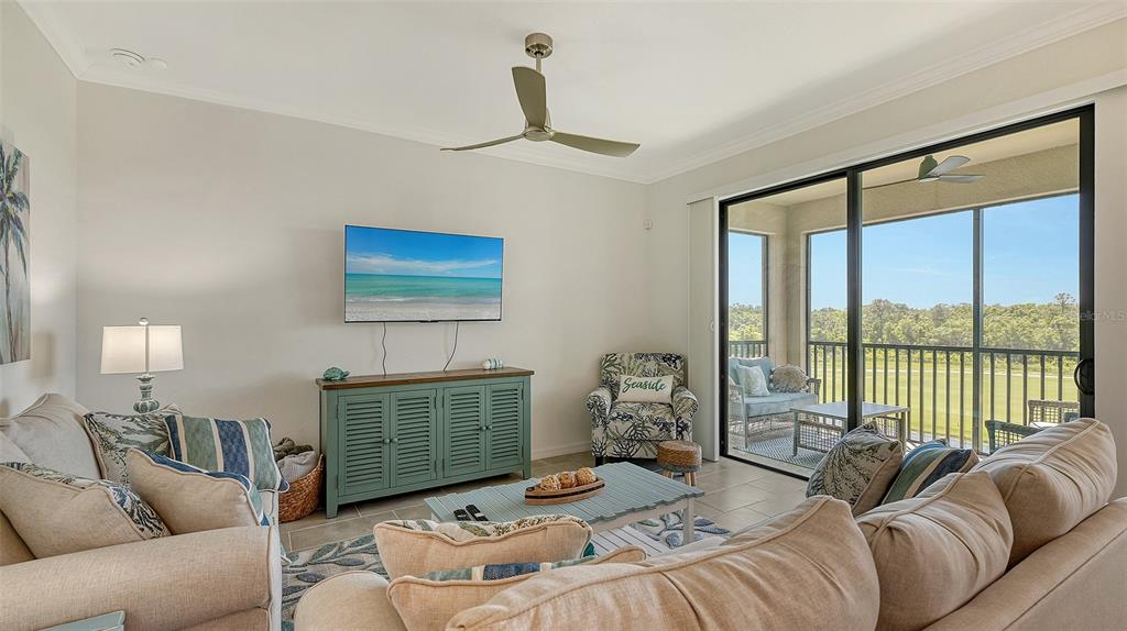 A living room features a blue media console, a patterned armchair, and a sliding glass door — 17902 GAWTHROP DRIVE UNIT 402, LAKEWOOD RANCH, FL