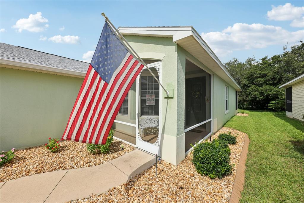 A light green house exterior features a screened-in entryway and an American flag — 4954 RAINBOW TROUT ROAD, TAVARES, FL