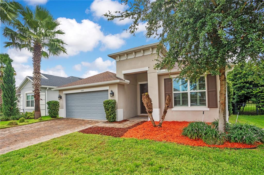 A single-story house with a gray garage, tan stucco exterior, and a landscaped front yard — 1103 NATHAN RIDGE RD, CLERMONT, FL