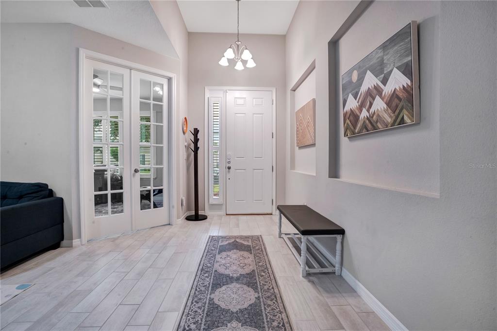 A bright entryway features light wood-look tile flooring, a white front door, and wall niches — 1103 NATHAN RIDGE RD, CLERMONT, FL