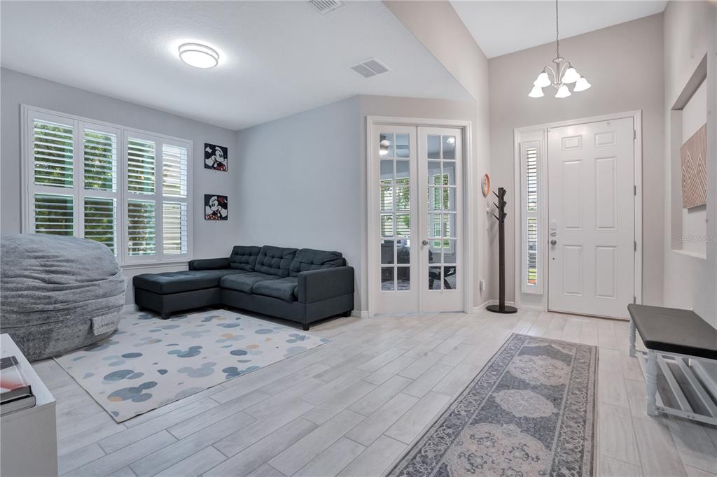 A living room features light wood-look tile flooring, a gray sectional sofa, and a front door — 1103 NATHAN RIDGE RD, CLERMONT, FL