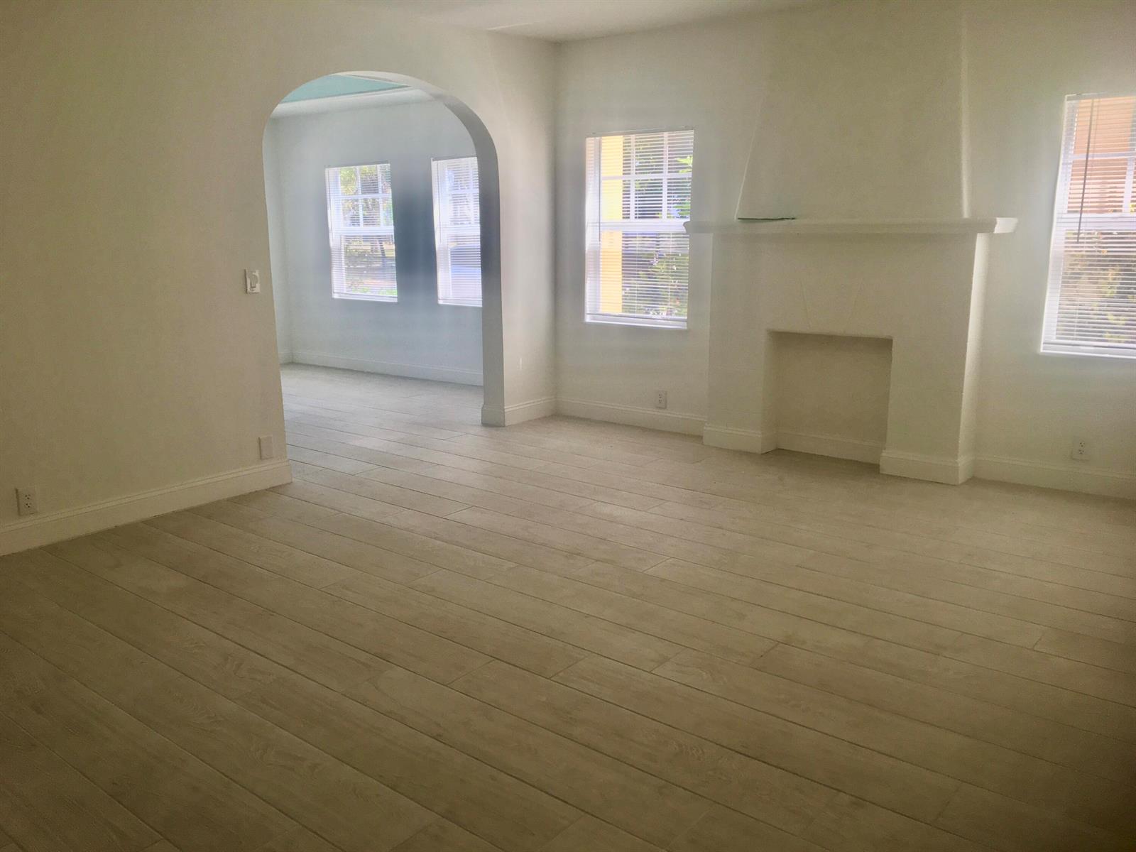 A bright living room features light wood-look flooring, white walls, an arched entryway, and a fireplace — 407 S Lakeside Drive, FL 33460, FL