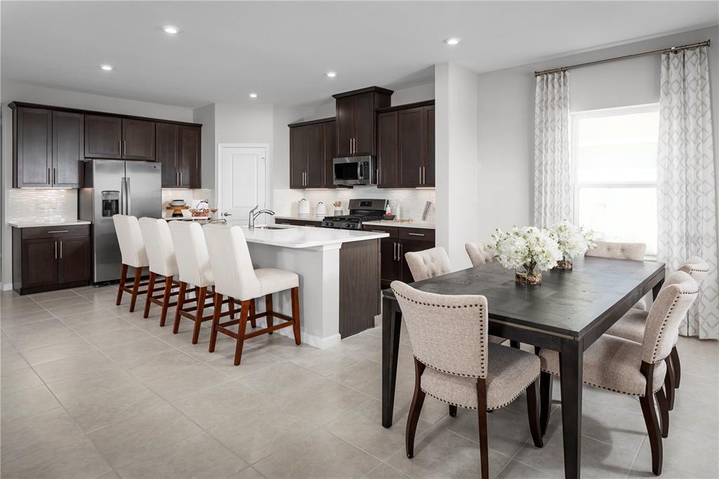 A kitchen with dark wood cabinets, a white island, and an adjacent dining area — 9812 PINE MILL COURT, CLERMONT, FL