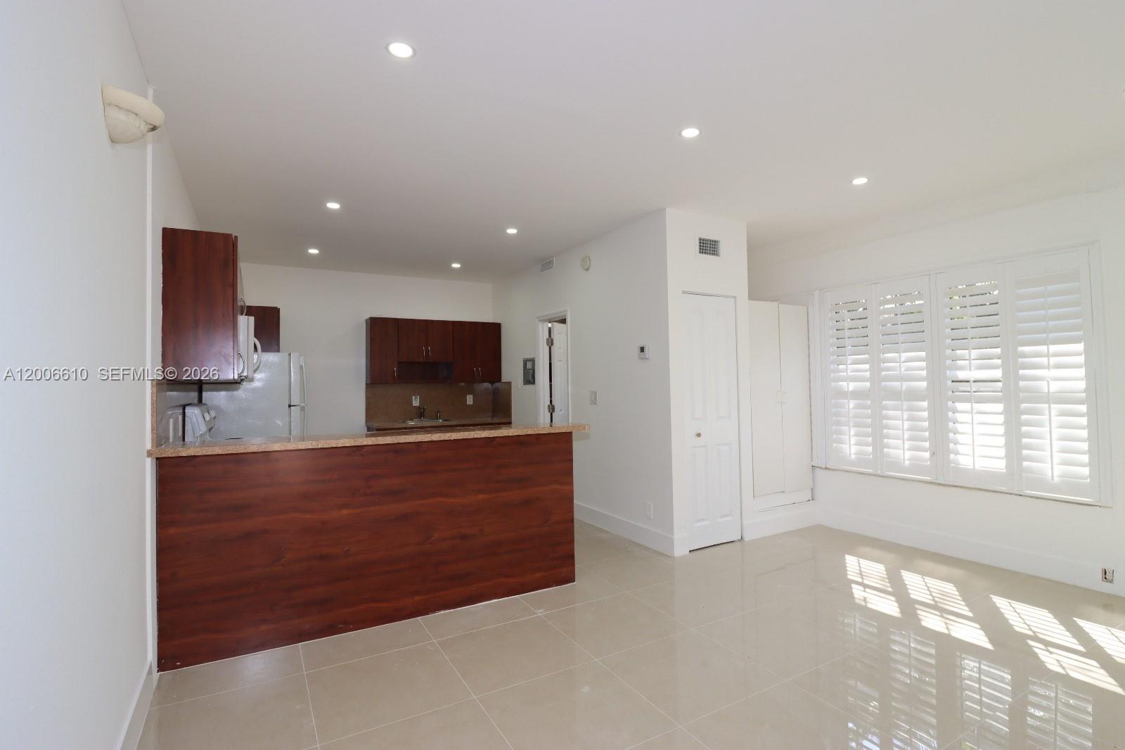 A kitchen with wood cabinets and a breakfast bar opens into a tiled living area — 2806 Taylor St # 0, Hollywood FL 33020, HOLLYWOOD, FL