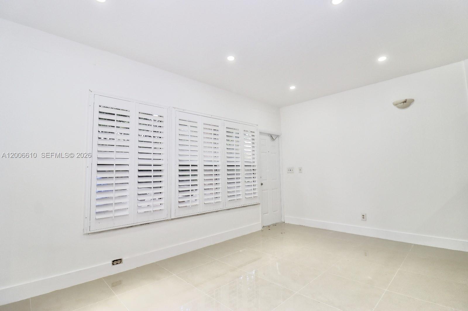 A bright, empty room features white walls, tiled floors, recessed lighting, and white plantation shutters — 2806 Taylor St # 0, Hollywood FL 33020, HOLLYWOOD, FL
