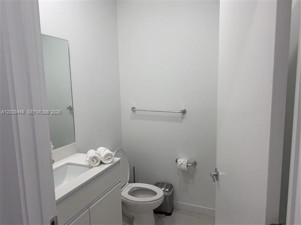 A small bathroom features a white vanity, a toilet, a mirror, and a towel bar — 2201 Polk St # 101, Hollywood FL 33020, HOLLYWOOD, FL