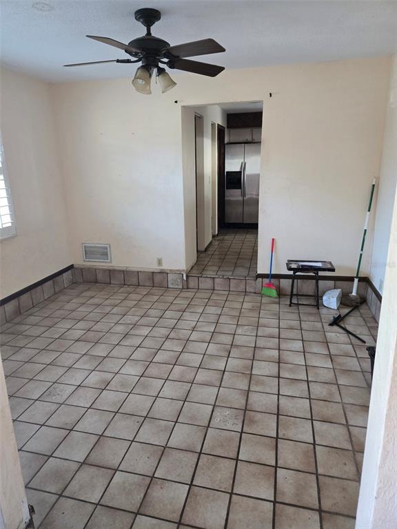 An empty room with tiled flooring, a ceiling fan, and a doorway leading to a kitchen — 748 MERRIMAC DRIVE, PORT ORANGE, FL