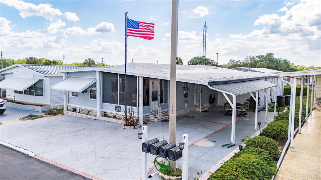 A light blue manufactured home features a screened porch, a carport, and an American flag — 7135 EL DEWITT STREET, ZEPHYRHILLS, FL