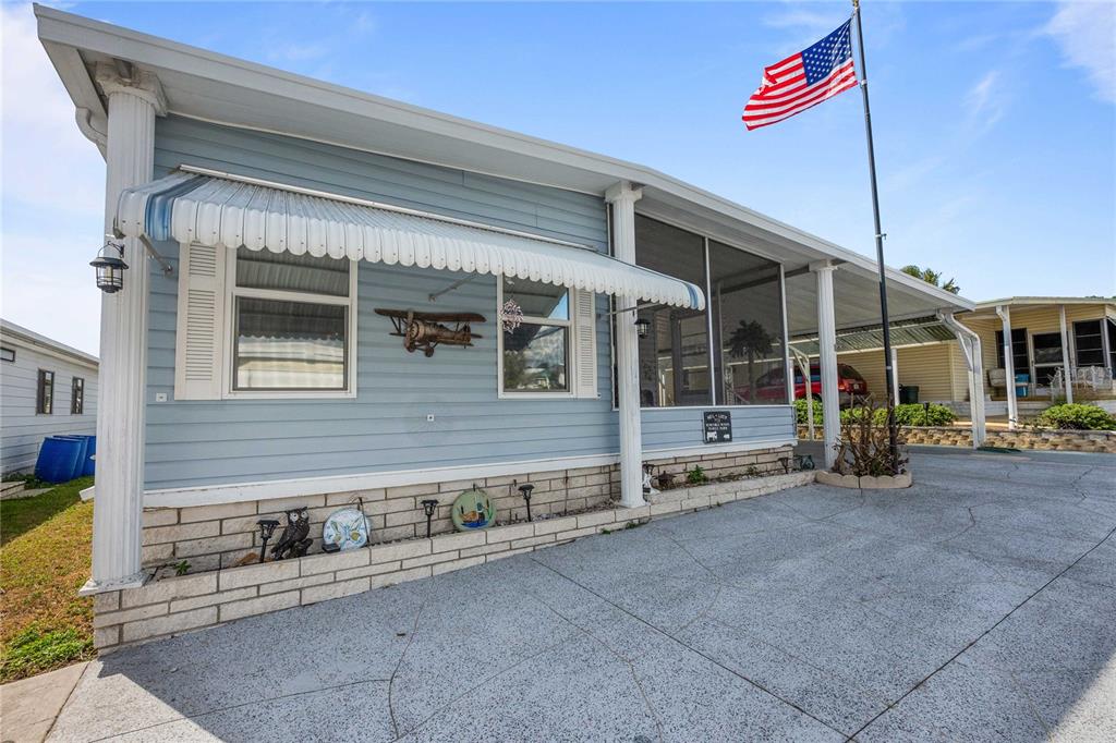 A light blue mobile home features a screened porch, a carport, and an American flag — 7135 EL DEWITT STREET, ZEPHYRHILLS, FL