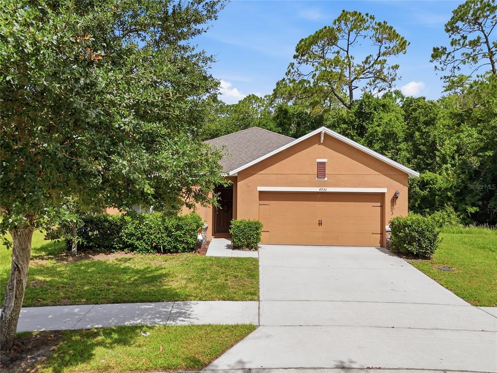A single-story house with a tan stucco exterior, a two-car garage, and a concrete driveway — 4930 HAROLD STANLEY DRIVE, KISSIMMEE, FL