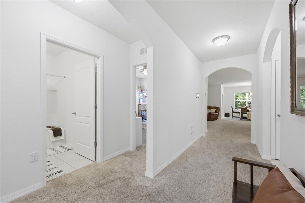 A hallway with beige carpet leads to a bathroom, a bedroom, and an open living area — 4930 HAROLD STANLEY DRIVE, KISSIMMEE, FL