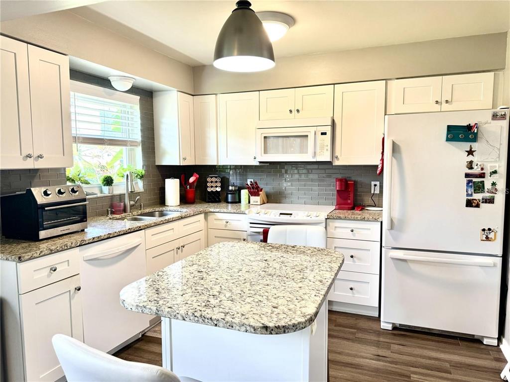A kitchen features white cabinets, granite countertops, a central island, and stainless steel appliances — 6997 VERSAILLES N UNIT n/a, PINELLAS PARK, FL