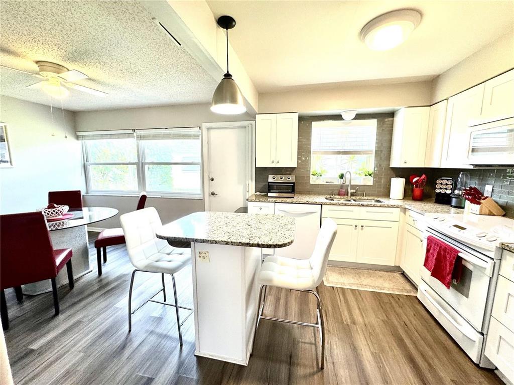 A kitchen and dining area feature white cabinets, granite countertops, and wood-look flooring — 6997 VERSAILLES N UNIT n/a, PINELLAS PARK, FL