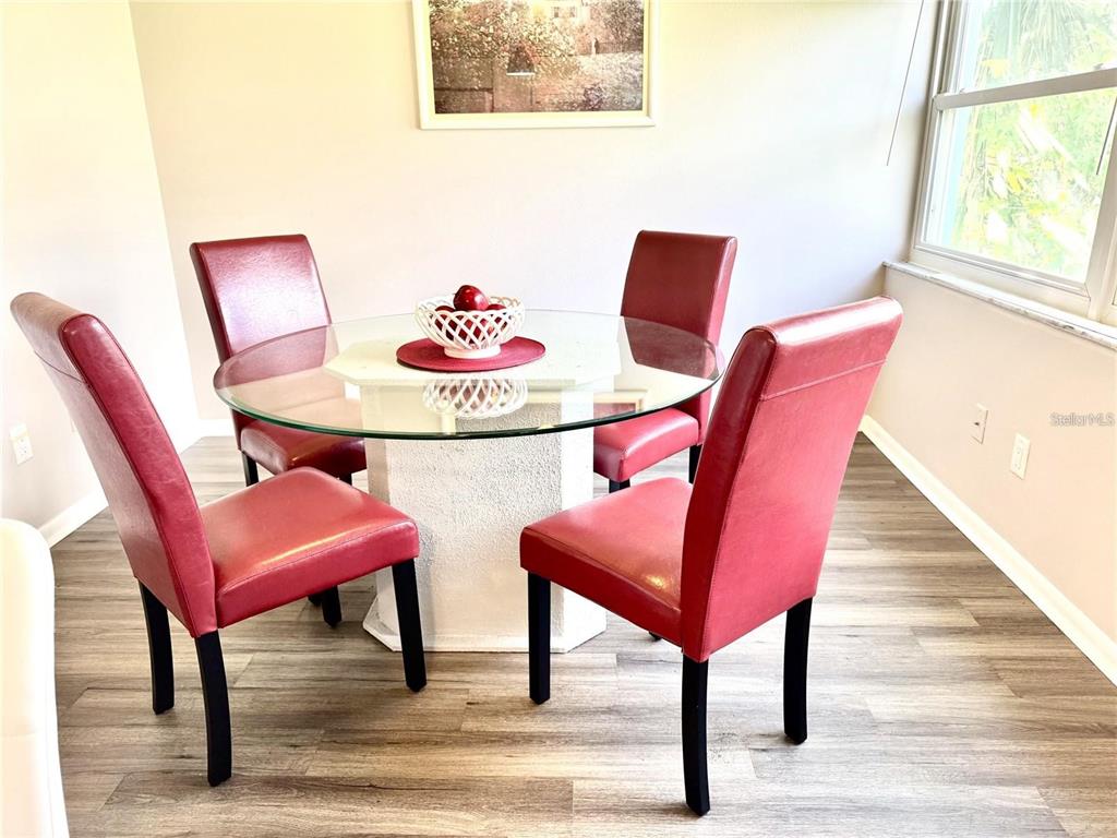 A dining area features a glass-topped table with four red chairs on wood-look flooring — 6997 VERSAILLES N UNIT n/a, PINELLAS PARK, FL