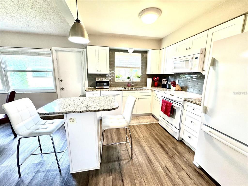 A kitchen features white cabinetry, granite countertops, a breakfast island, and wood-look flooring — 6997 VERSAILLES N UNIT n/a, PINELLAS PARK, FL