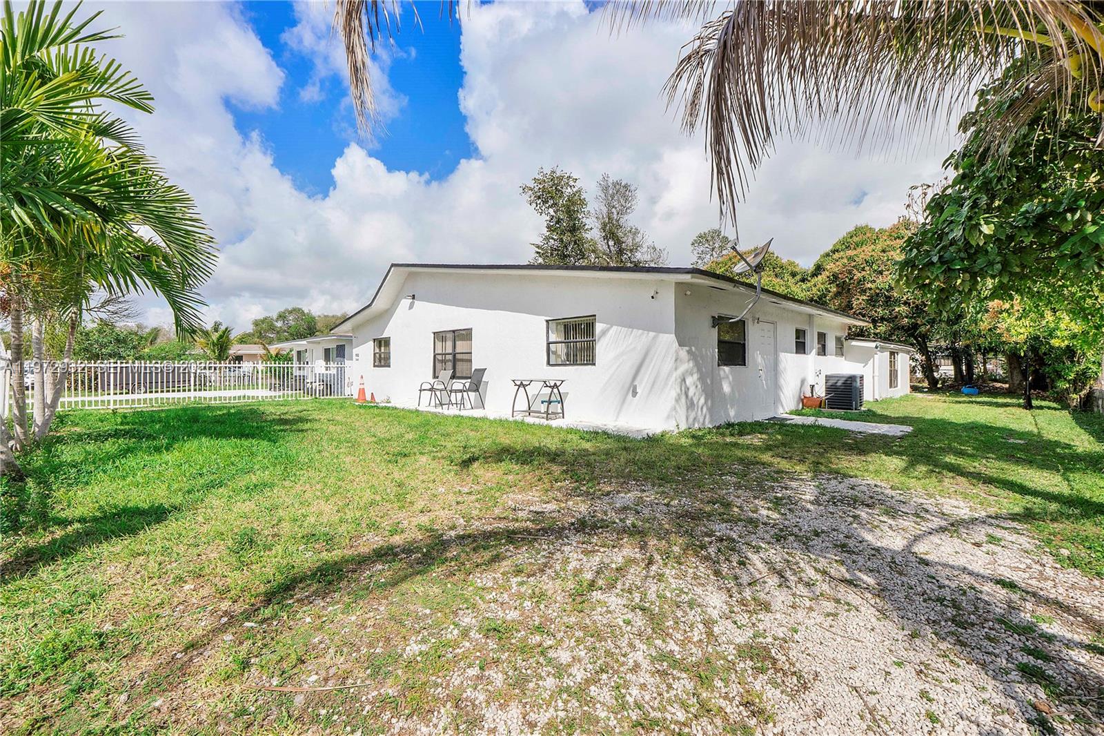The exterior of a white, single-story house with a gravel driveway and palm trees — 1563 NE 148th St, Miami FL 33161, MIAMI, FL