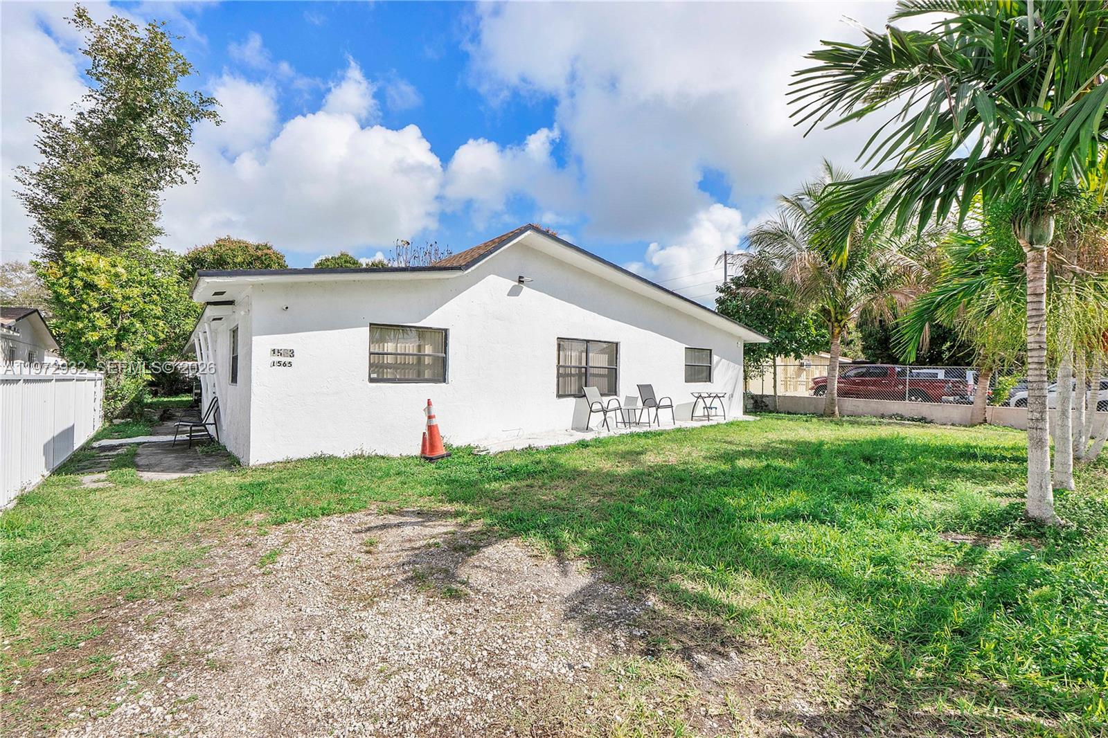 The exterior of a white, single-story house features a gravel driveway and a grassy yard — 1563 NE 148th St, Miami FL 33161, MIAMI, FL