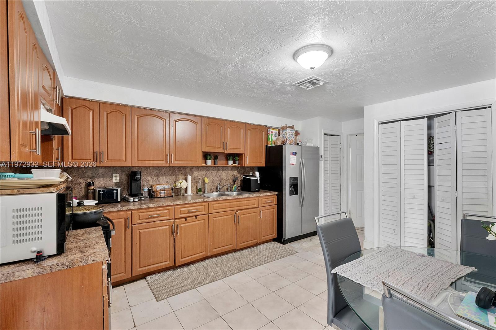 A kitchen features wood cabinets, laminate countertops, a stainless steel refrigerator, and tiled flooring — 1563 NE 148th St, Miami FL 33161, MIAMI, FL