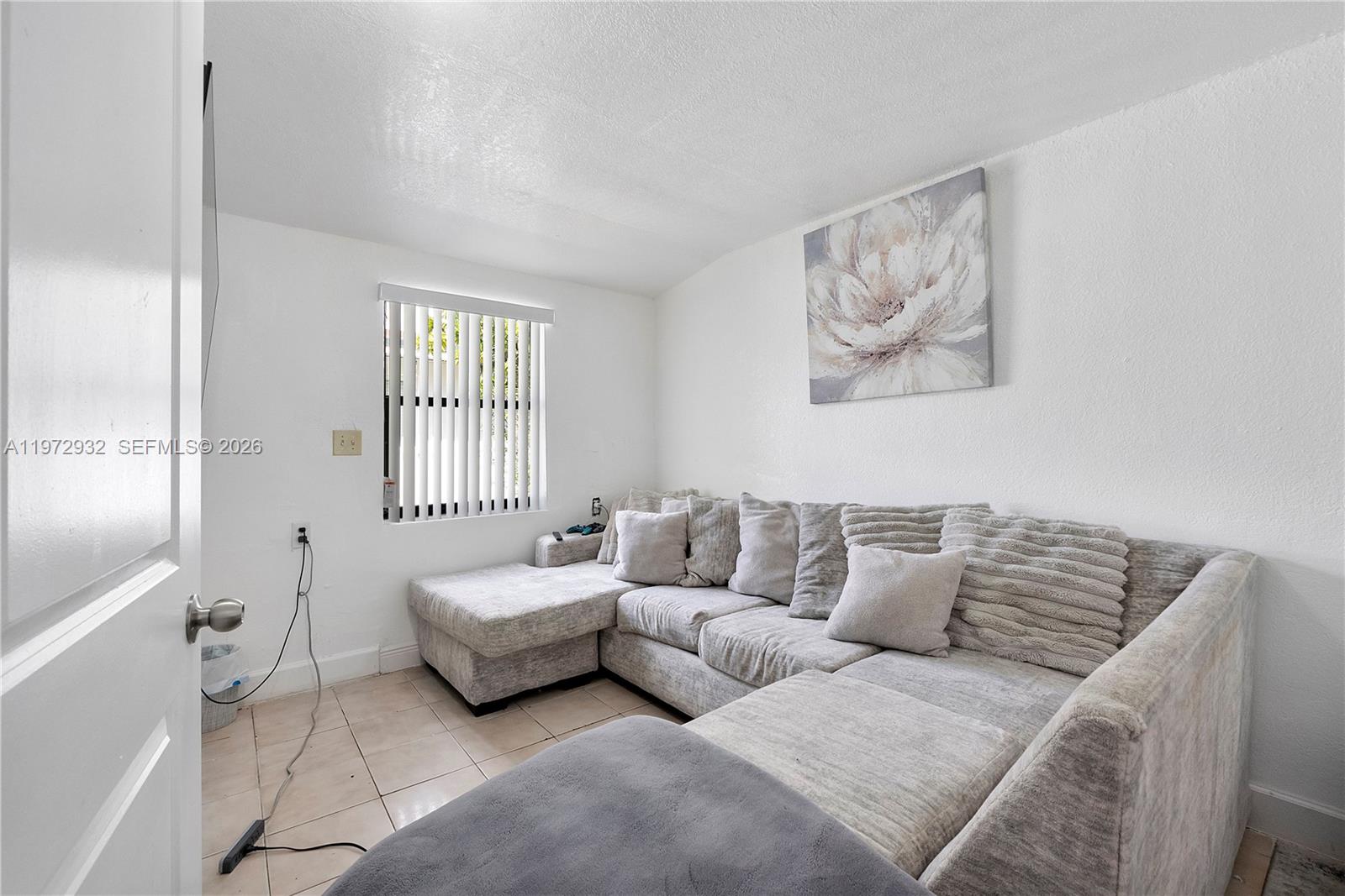 A small room features a large gray sectional sofa, tiled floors, and a window — 1563 NE 148th St, Miami FL 33161, MIAMI, FL