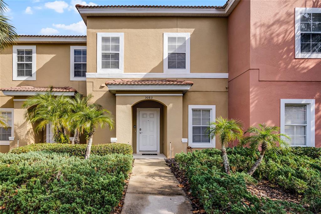 The exterior of a two-story tan townhouse features a white front door and landscaping — 3083 YELLOW LANTANA LANE, KISSIMMEE, FL