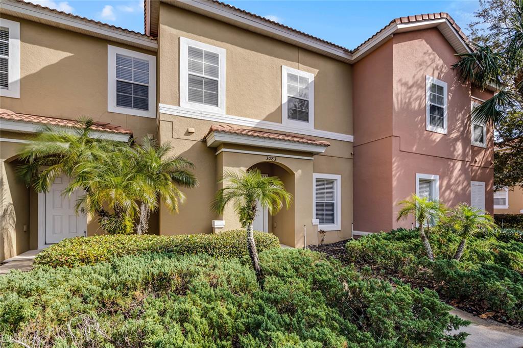 A two-story tan and peach townhouse exterior with palm trees and a landscaped front yard — 3083 YELLOW LANTANA LANE, KISSIMMEE, FL