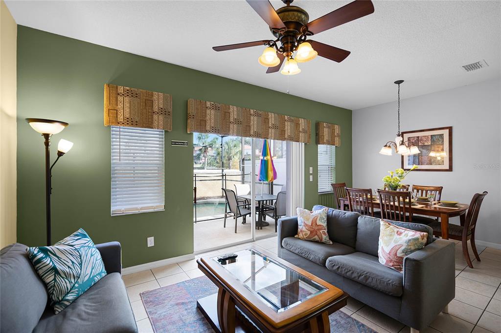 A living room with a gray sofa, coffee table, and dining area overlooking a pool patio — 3083 YELLOW LANTANA LANE, KISSIMMEE, FL