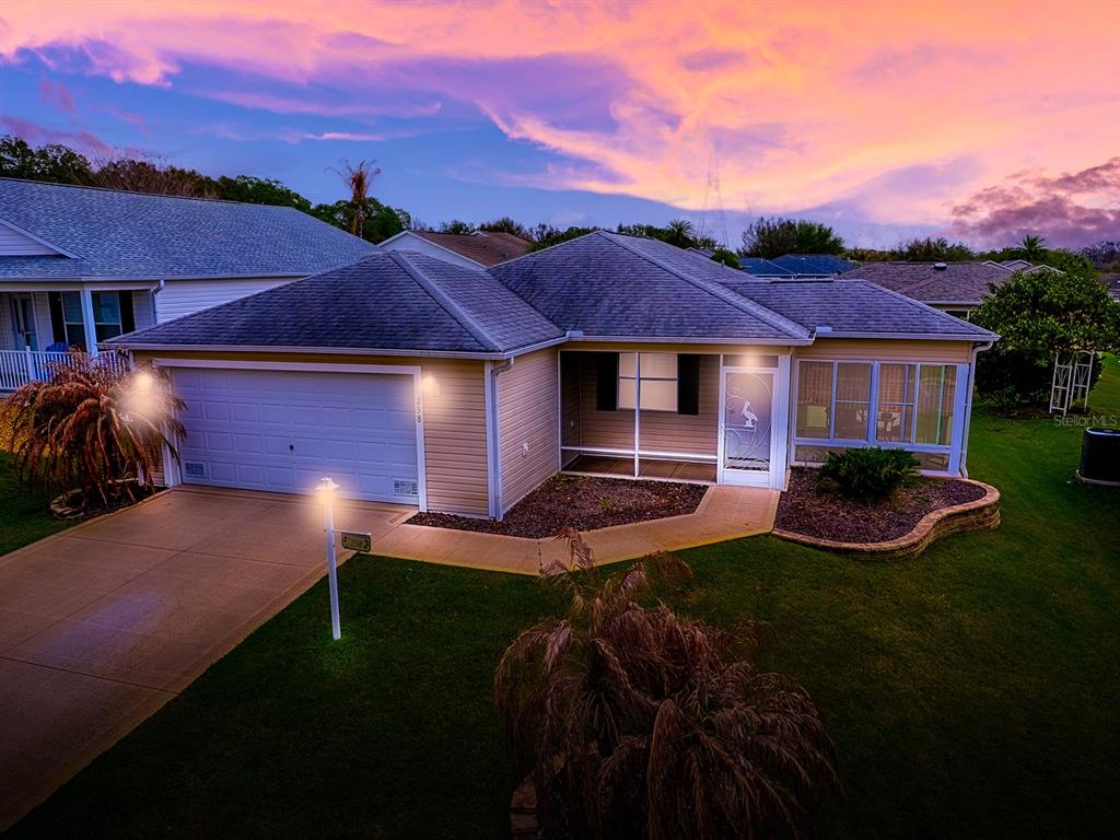 A single-story house with a two-car garage, a screened entryway, and a sunset sky — 258 ARBELLA LOOP, THE VILLAGES, FL