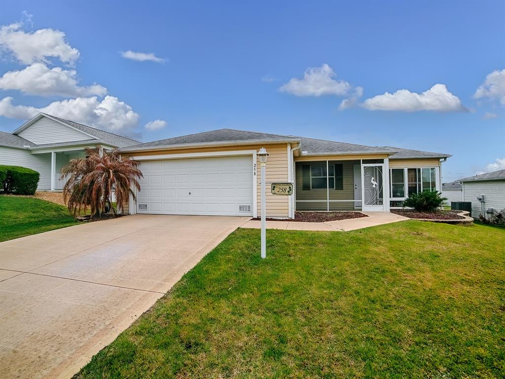 A single-story house with a two-car garage, a screened entryway, and a concrete driveway — 258 ARBELLA LOOP, THE VILLAGES, FL