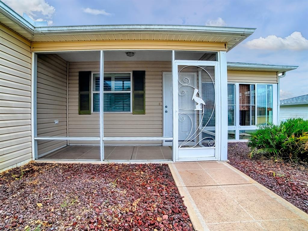A screened-in front porch features tan siding, a white storm door, and a concrete walkway — 258 ARBELLA LOOP, THE VILLAGES, FL