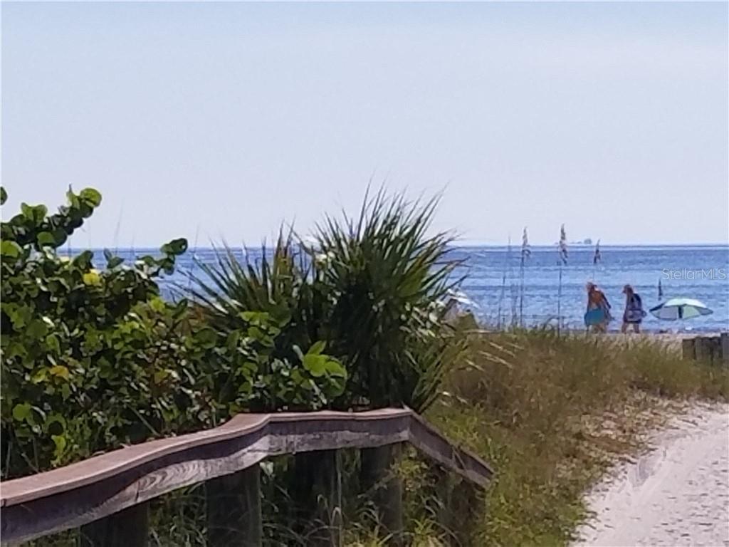 A wooden boardwalk leads through coastal vegetation toward a beach with people and the ocean — 504 67TH AVENUE UNIT 12, ST PETE BEACH, FL