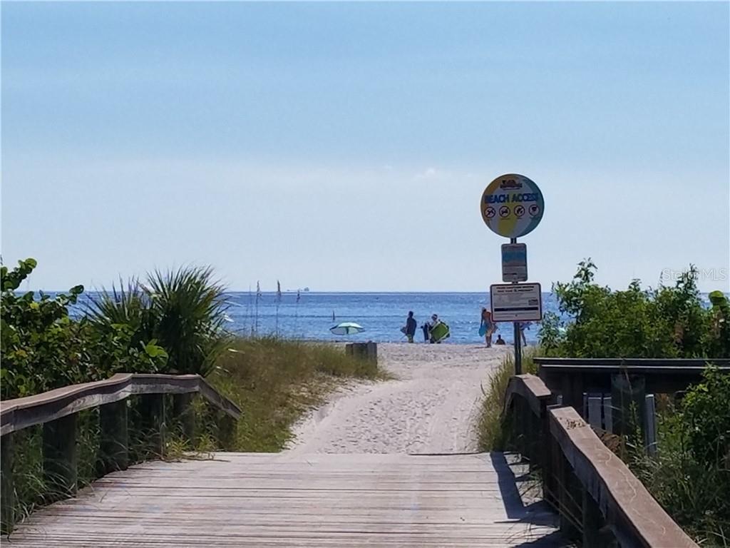 A wooden boardwalk leads through sand dunes to a beach with a public access sign — 504 67TH AVENUE UNIT 12, ST PETE BEACH, FL