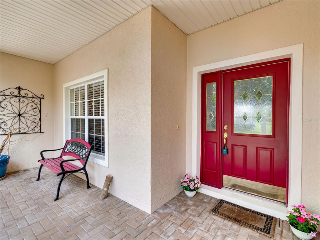 A covered front porch features a red door, a matching bench, and a brick floor — 478 BALBOA DRIVE, KISSIMMEE, FL