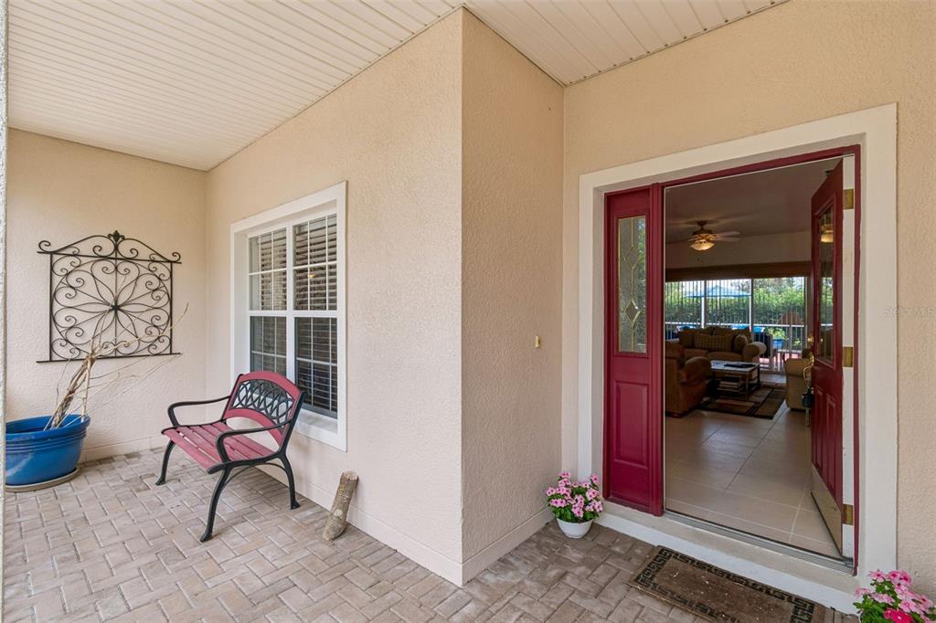 A covered brick porch features a red bench, wall decor, and an open front door — 478 BALBOA DRIVE, KISSIMMEE, FL
