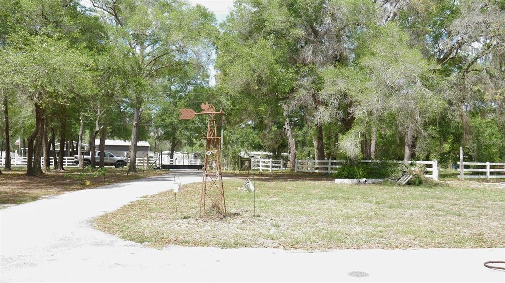 A gravel driveway leads to a metal windmill ornament in a tree-lined yard — 17622 CAUFIELD ROAD, SPRING HILL, FL