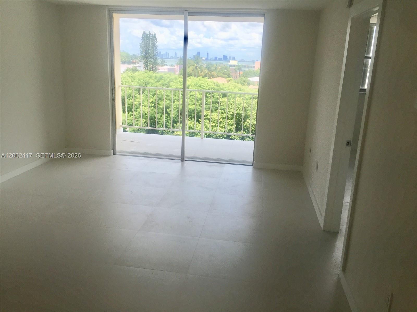 An empty room features light-colored tile flooring, white walls, and a sliding glass door balcony — 6900 Bay Dr # 5A, Miami Beach FL 33141, MIAMI BEACH, FL
