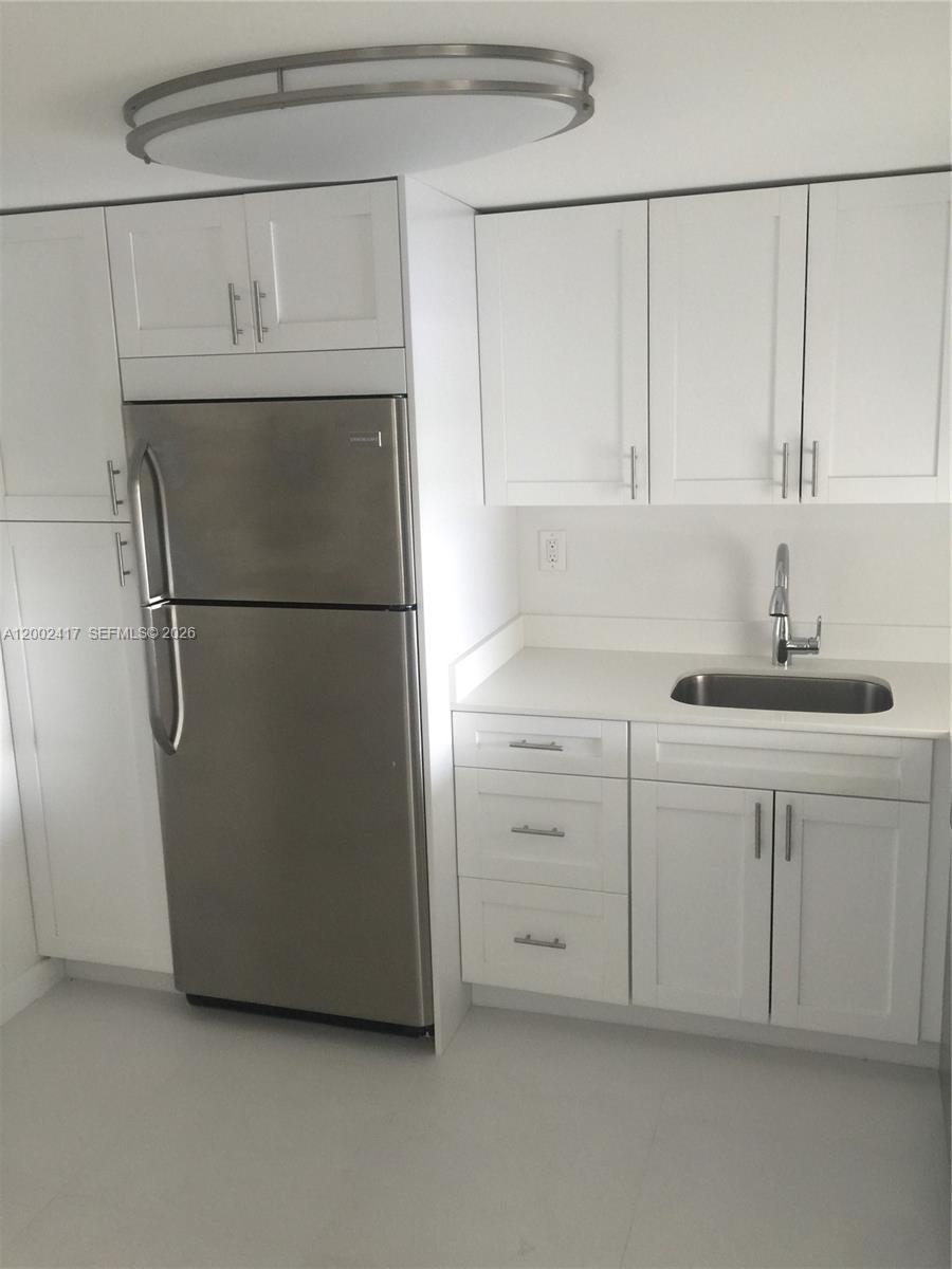 A small kitchen features white cabinets, a stainless steel refrigerator, and a sink — 6900 Bay Dr # 5A, Miami Beach FL 33141, MIAMI BEACH, FL