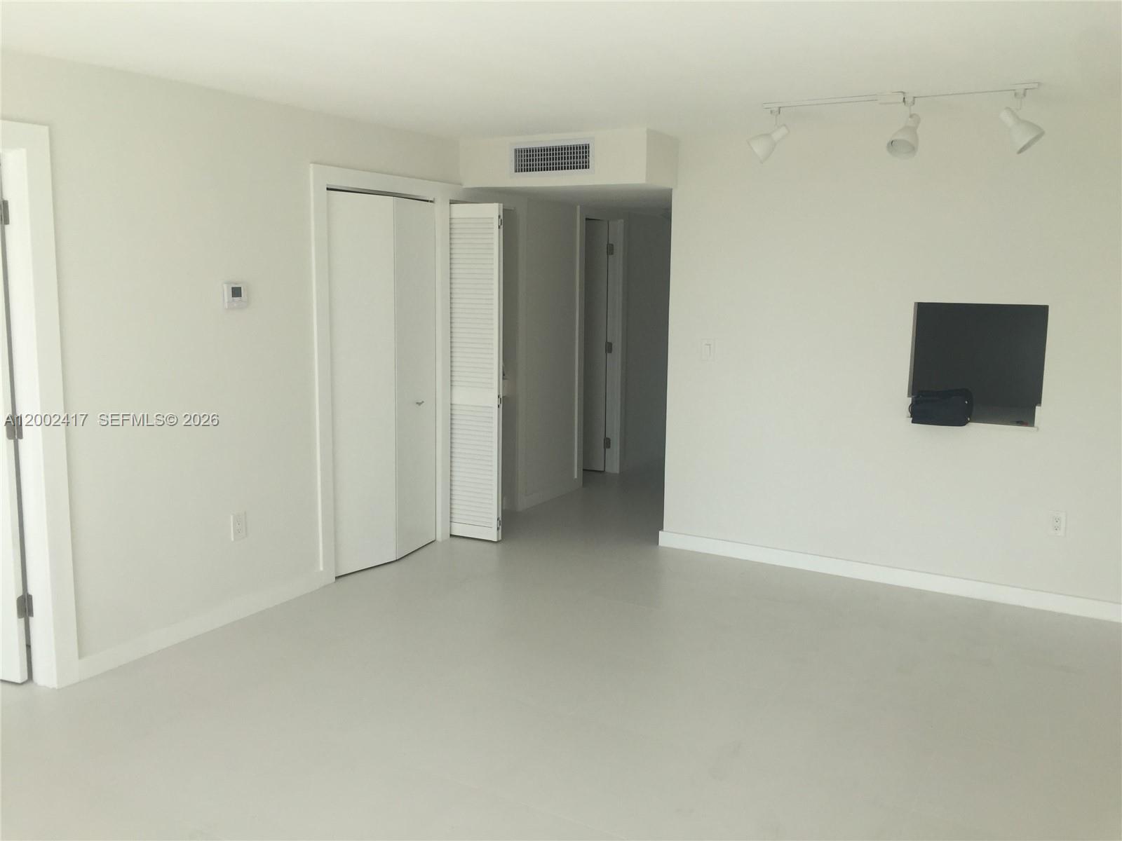 A minimalist room features white walls, light flooring, a wall-mounted television, and track lighting — 6900 Bay Dr # 5A, Miami Beach FL 33141, MIAMI BEACH, FL