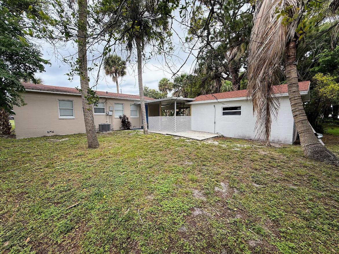 A view of the backyard showing a tan house, a white addition, and palm trees — 1010 Mayflower Road, Fort Pierce FL 34950, FORT PIERCE, FL