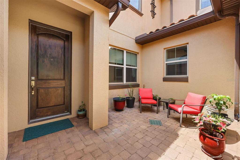 A paved courtyard features a wooden front door, two red chairs, and several potted plants — 16614 HARBOR SAIL WAY, WINTER GARDEN, FL