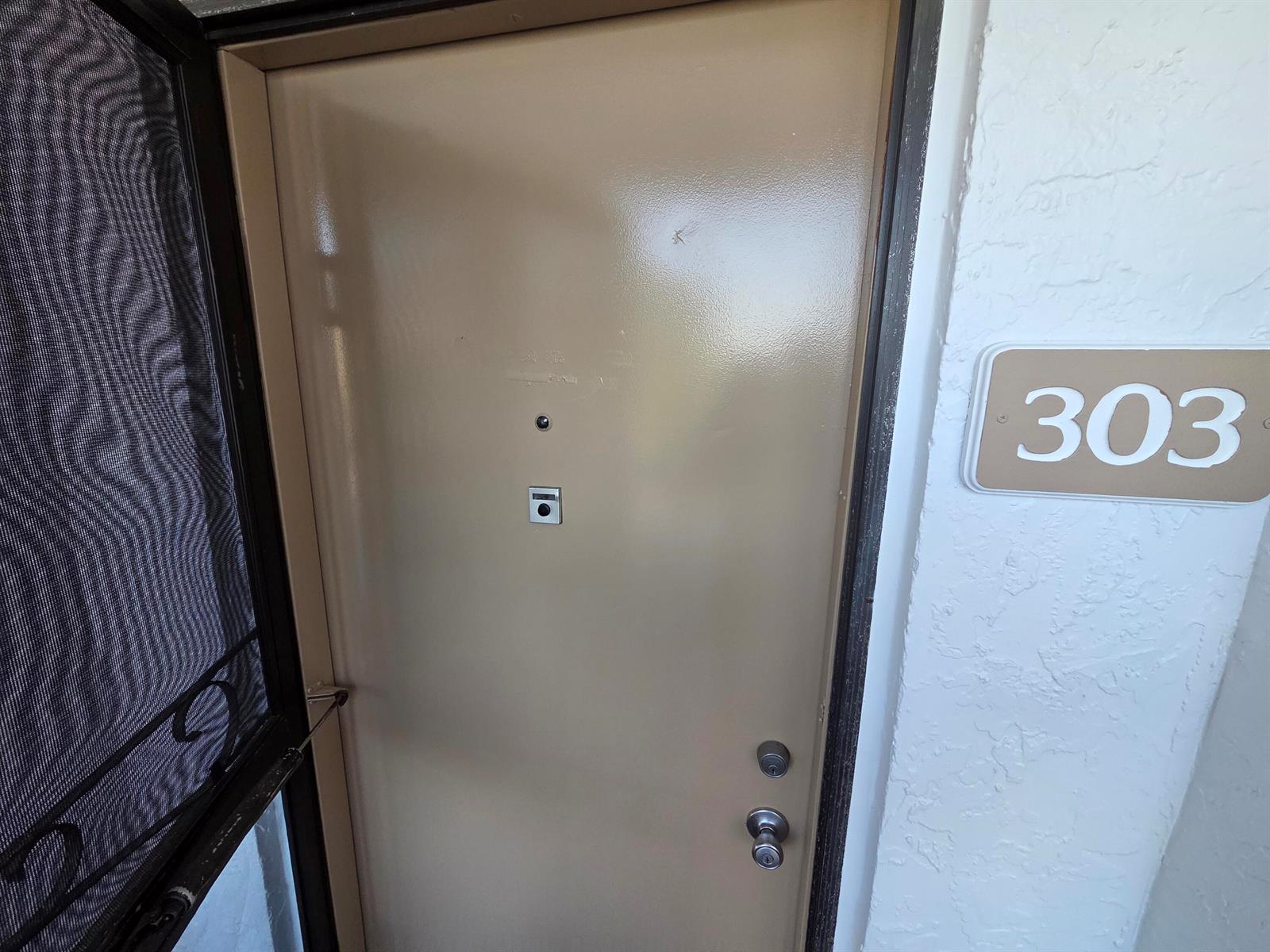 A beige apartment door labeled 303 features a peephole, a door knocker, and two locks — 4770 Fountains Drive S # 303, FL 33467, FL