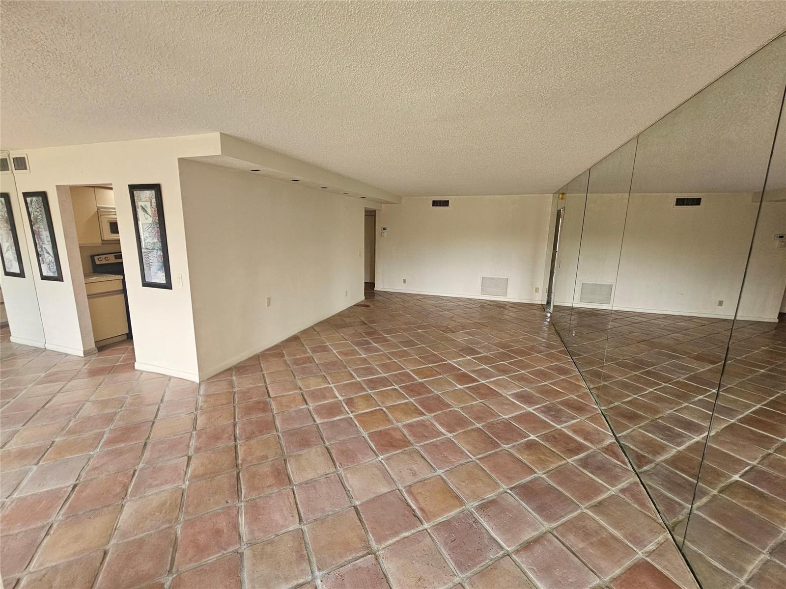 An empty room features terracotta tile flooring, a mirrored wall, and a recessed kitchen area — 4770 Fountains Drive S # 303, FL 33467, FL