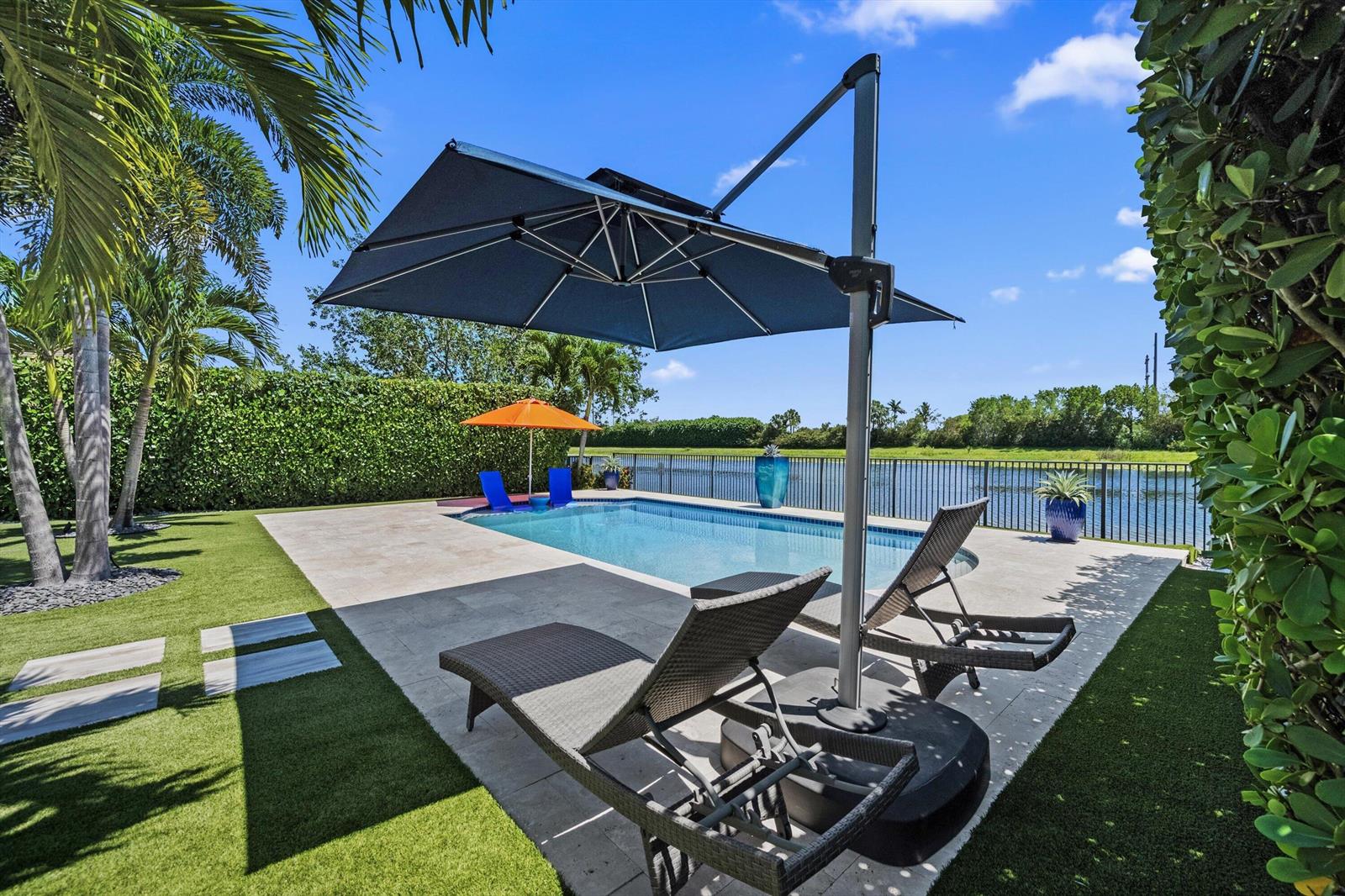 A backyard pool area features lounge chairs, a large umbrella, and a view of water — 8779 Grand Prix Lane, Boynton Beach FL 33472, BOYNTON BEACH, FL