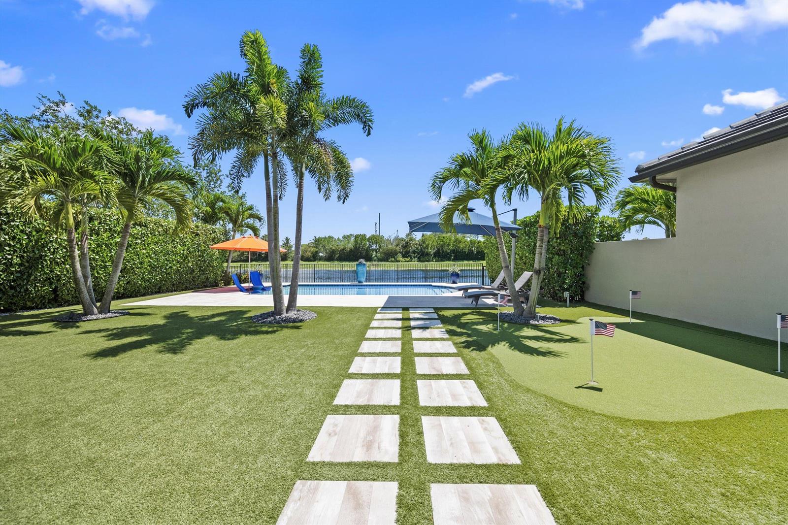 A backyard features a swimming pool, a putting green, palm trees, and a stone walkway — 8779 Grand Prix Lane, Boynton Beach FL 33472, BOYNTON BEACH, FL