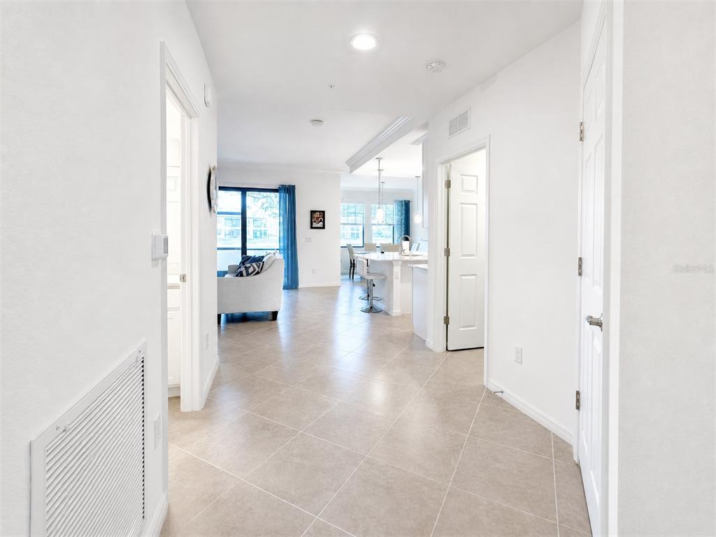 A bright hallway with tile flooring leads to an open-concept kitchen and living area — 10054 CROOKED CREEK DRIVE UNIT 102, VENICE, FL